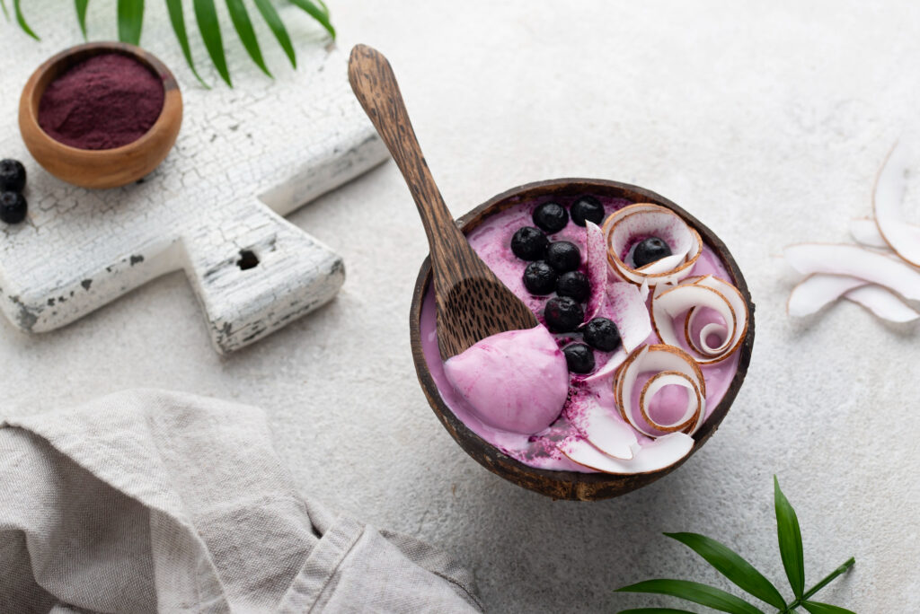 A bowl of açai smoothie topped with blueberries and coconut shavings on a rustic white surface.