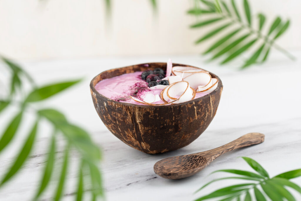 Açai smoothie bowl with coconut flakes and blueberries served in a rustic coconut shell bowl.