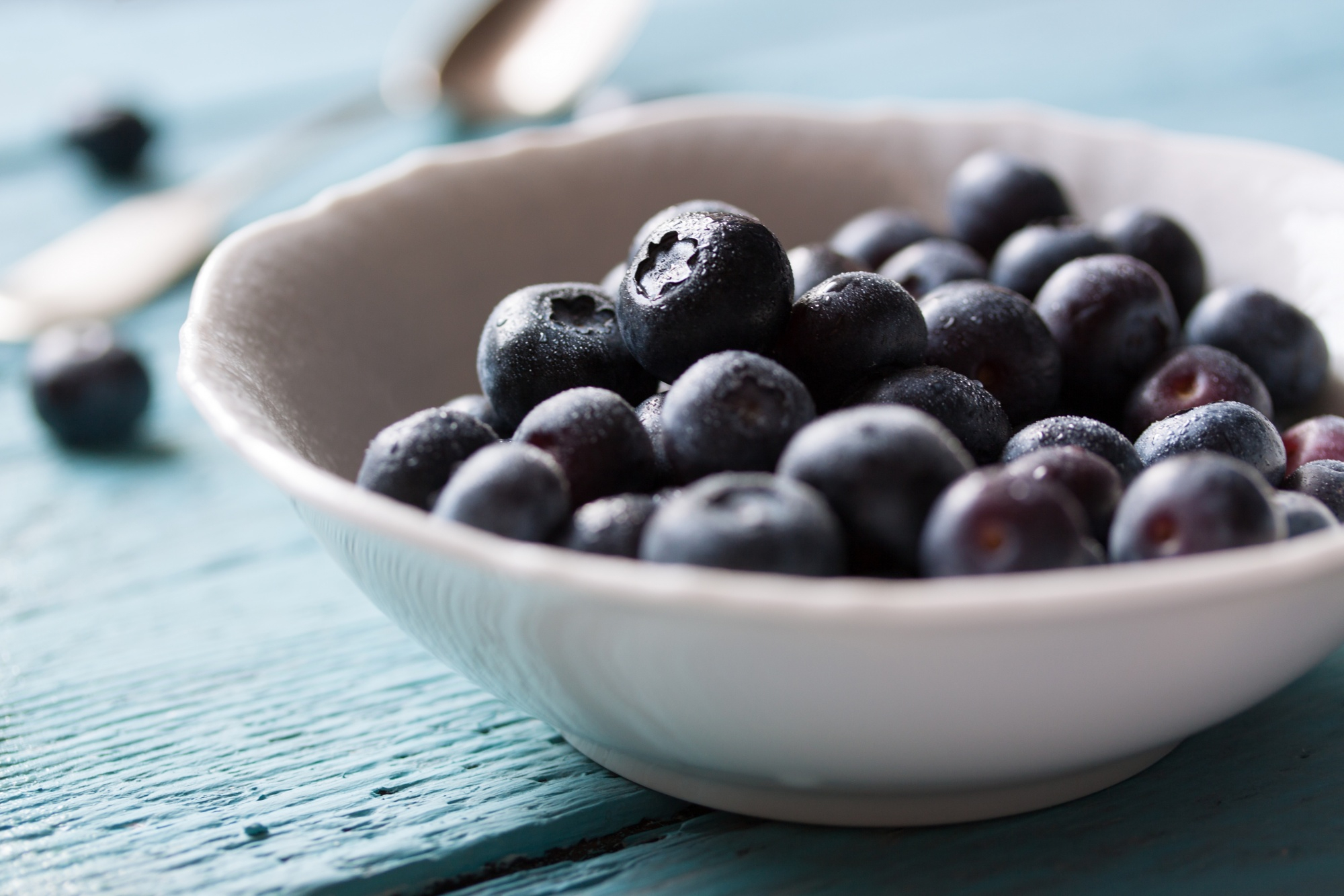 A white bowl filled with fresh açai berries, glistening with natural freshness on a blue table.