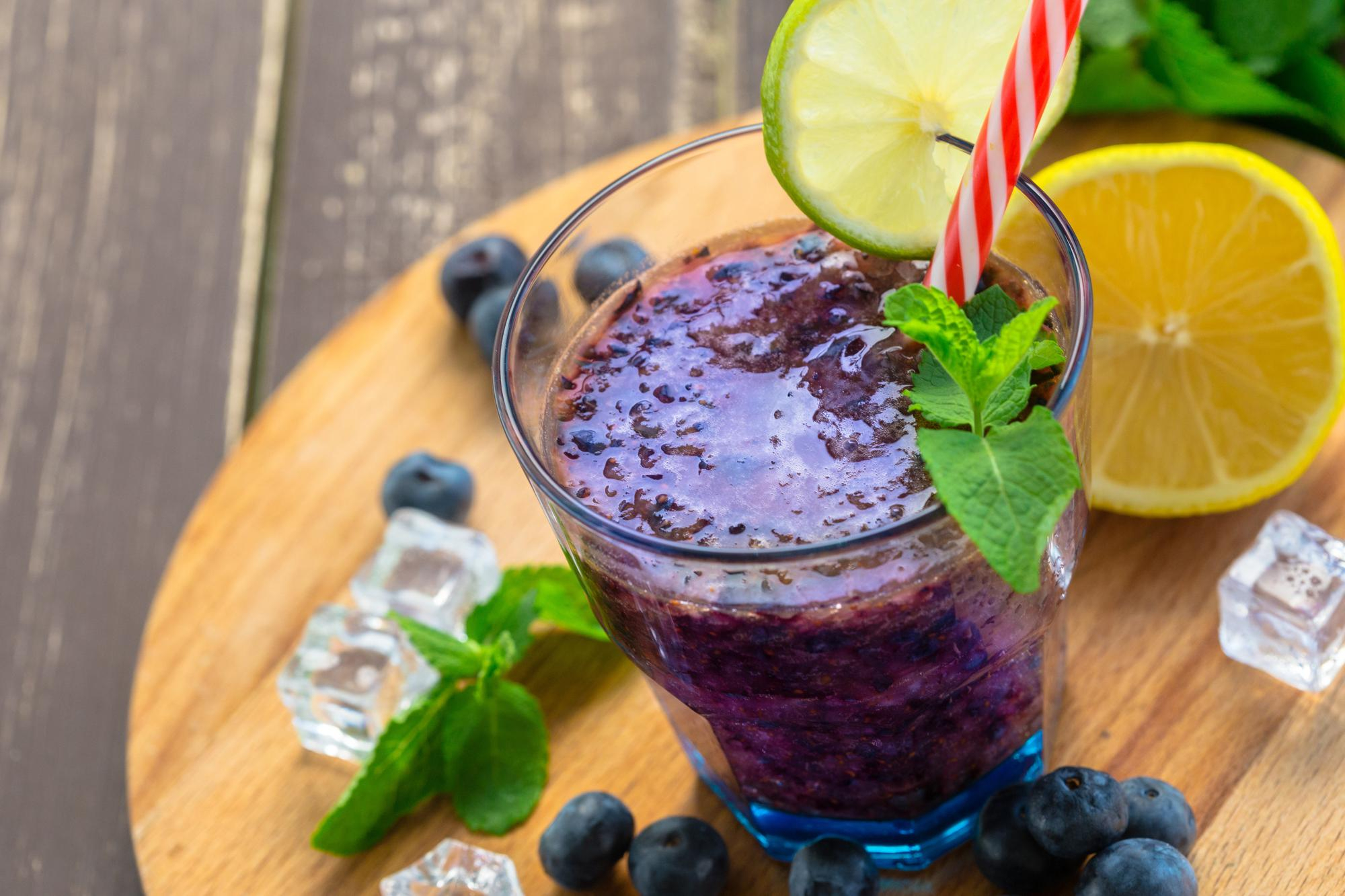 A refreshing Healthy Food smoothie with blueberries, lime, and mint on a wooden board.