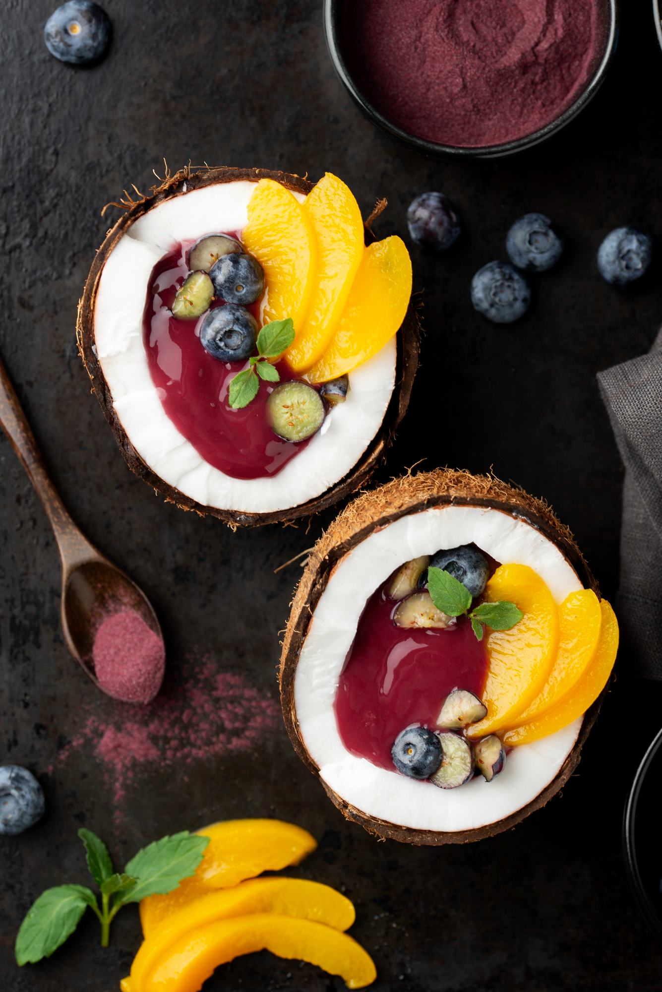 Exotic açaí bowl served in a coconut shell with peaches, blueberries, and mint – gourmet organic superfood