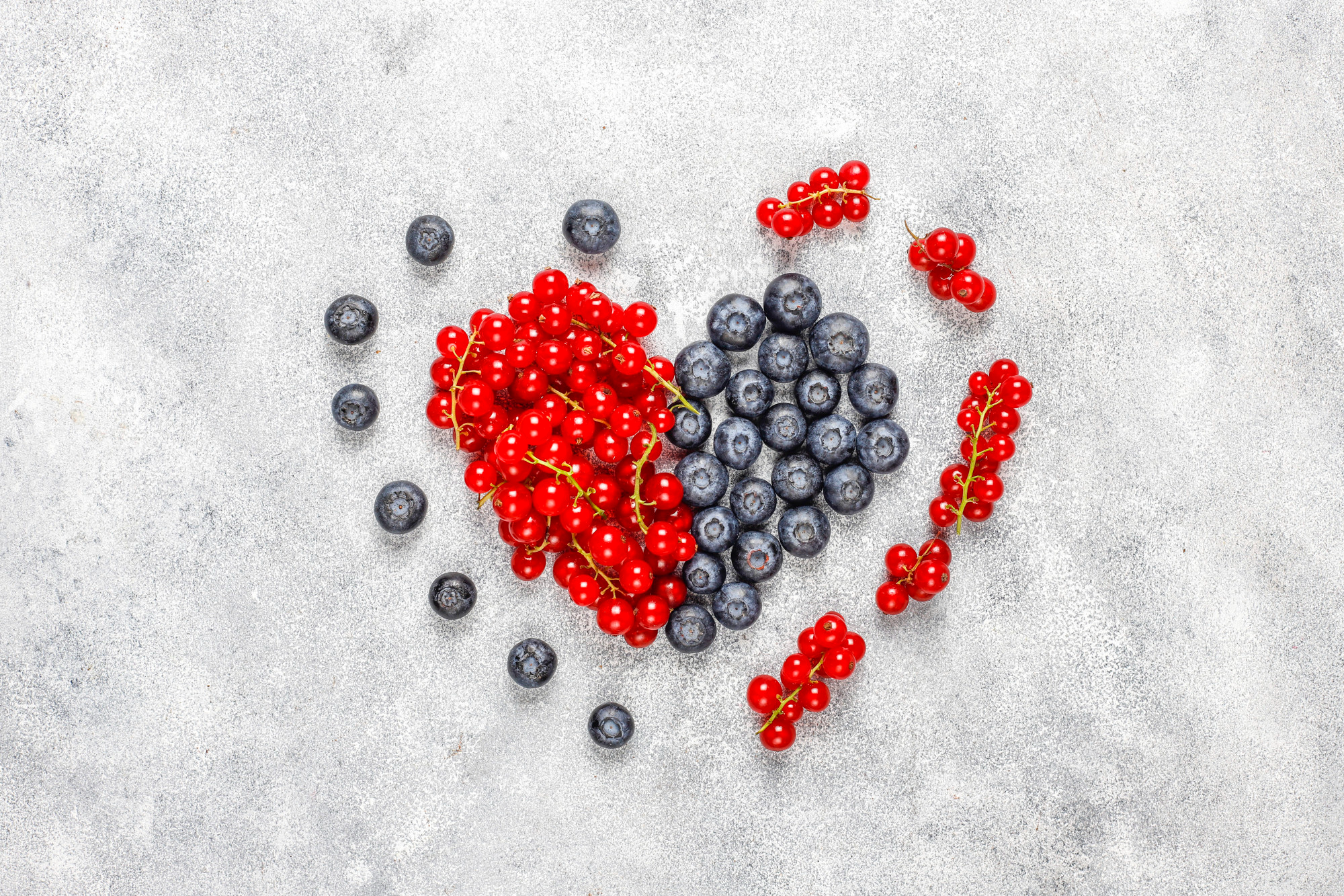 Heart-shaped arrangement of red currants and blueberries showcasing natural açaí antioxidants and anthocyanins on white surface