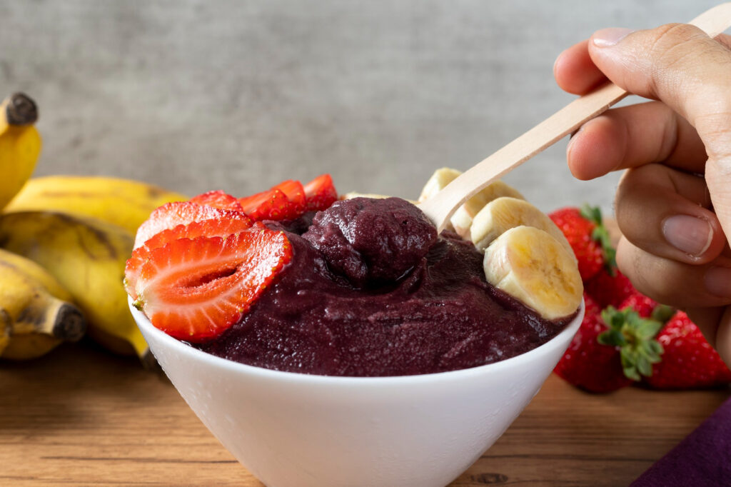 Purple açaí bowl with strawberries and banana slices being eaten with wooden spoon, rich in açaí antioxidants