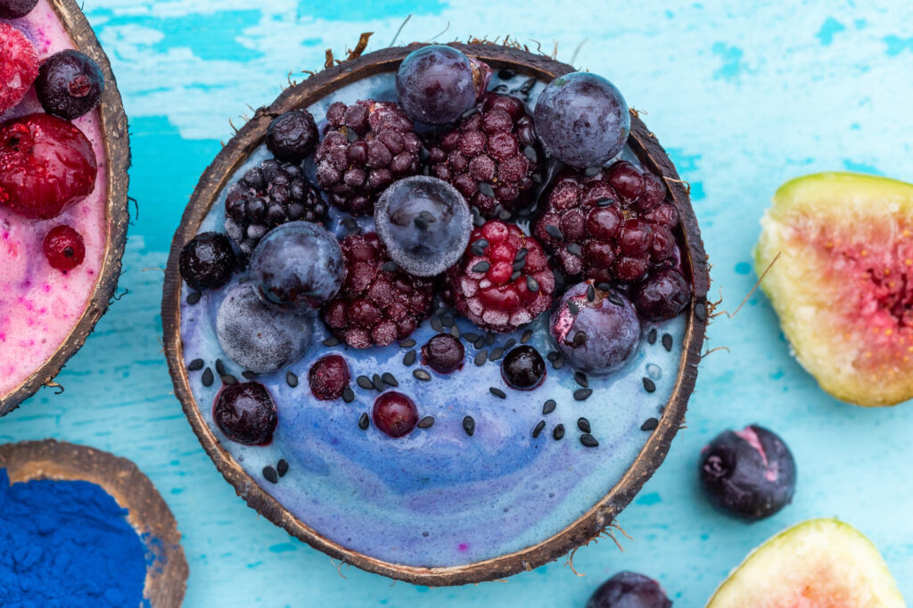 Coconut bowl with blue açaí smoothie topped with berries and seeds, maximizing açaí antioxidants absorption