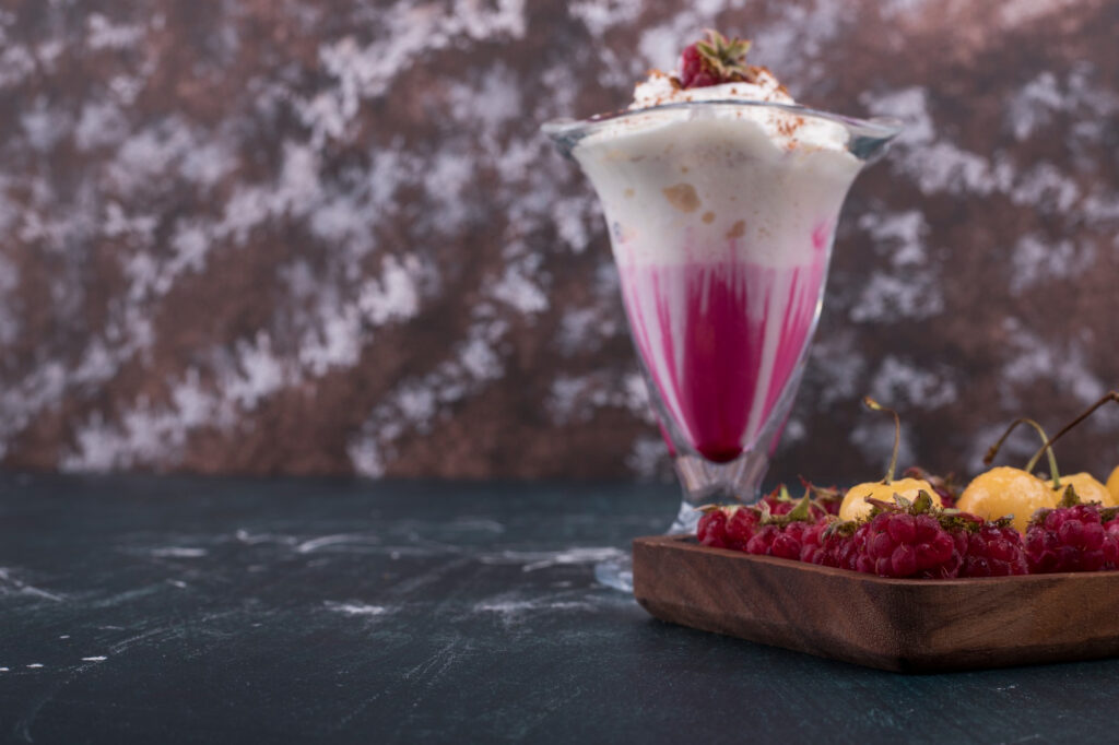 Elegant açaí gastronomy dessert glass showcasing layered pink açaí preparation with cream, accompanied by fresh berries on dark marble surface