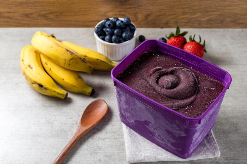 Purple açaí puree in container with bananas and fresh fruits for premium healthy food delivery