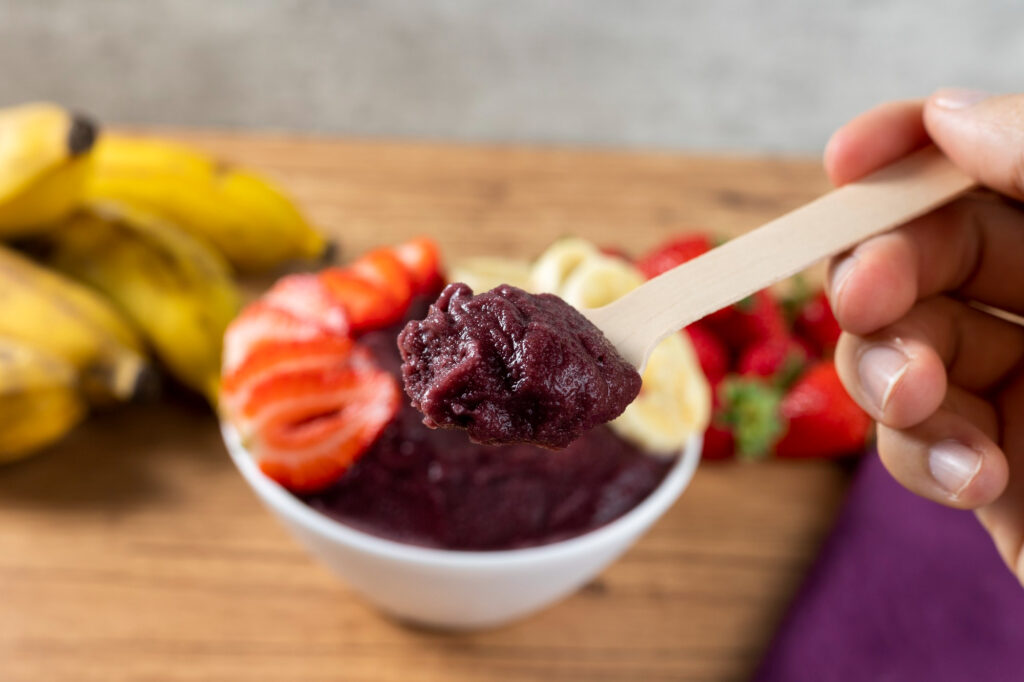 Spoon of organic açaí puree with fresh fruits background for artisanal healthy food delivery