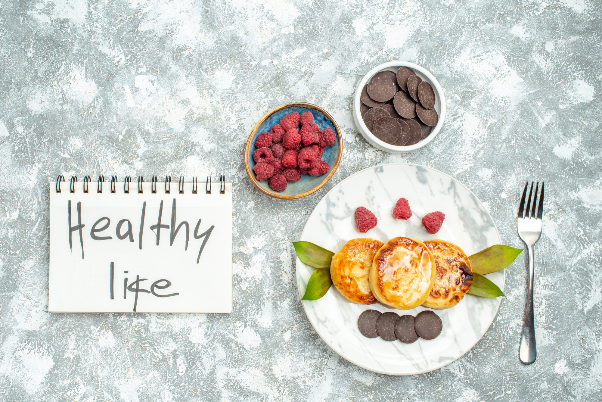 Microbiome diet healthy breakfast with raspberries, chocolate coins and pancakes on marble surface with "Healthy Life" notebook